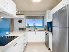 Eine moderne Küche mit Einbauherd, Edelstahlkühlschrank und Meerblick durch ein großes Fenster.