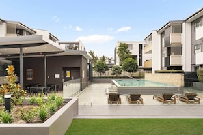 Ein moderner Außenpoolbereich mit Liegestühlen, einer überdachten Lounge und einer Steinmauer.