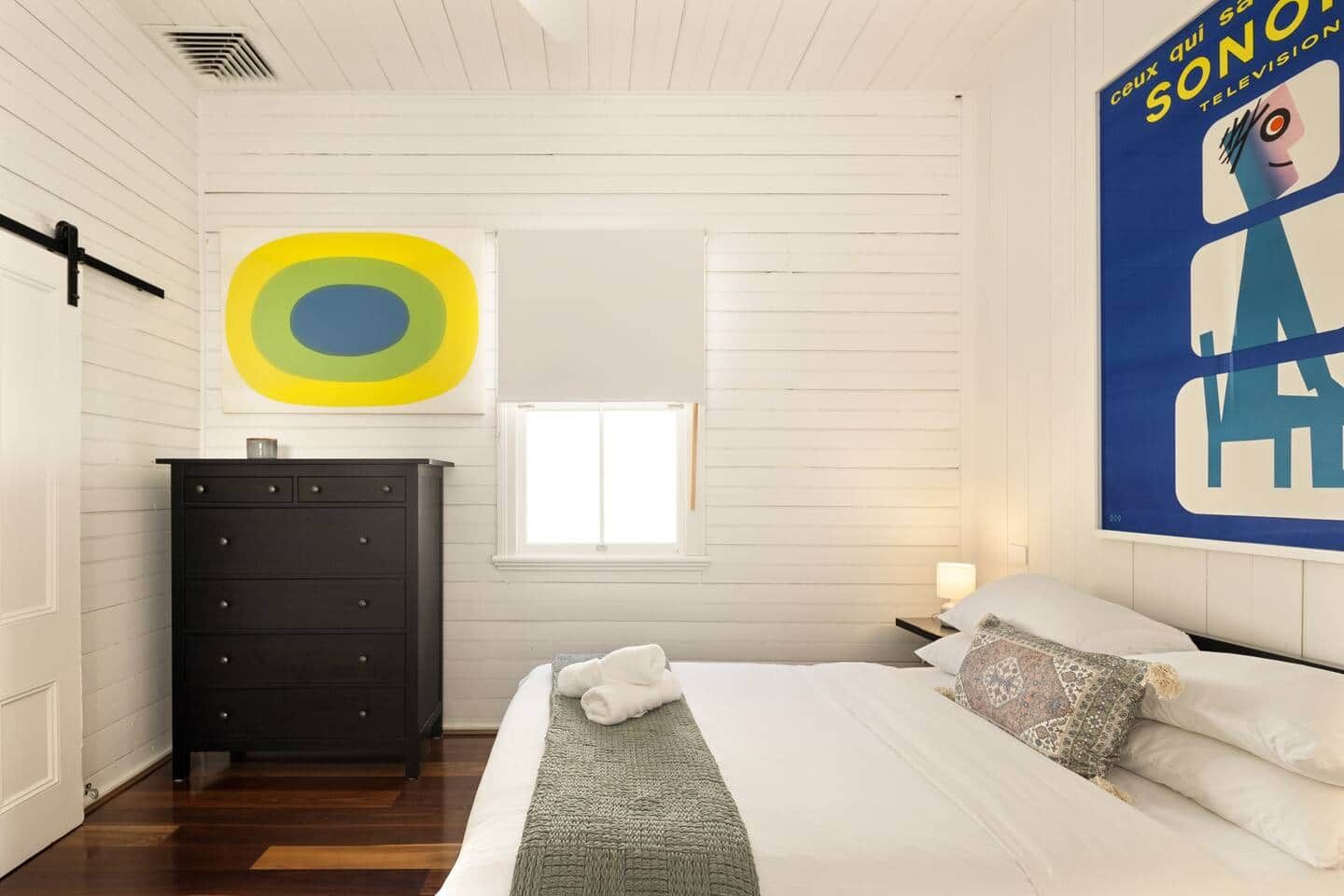 A bedroom with a bed, a dresser, a window, and a poster on the wall.