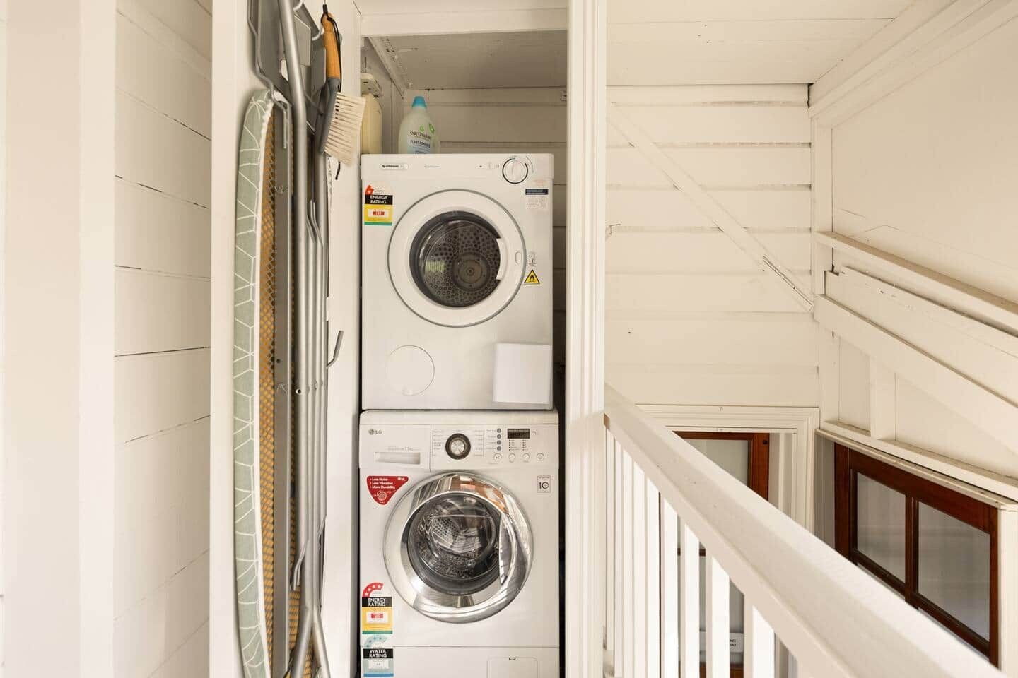 A laundry room with two stacked washing machines, a drying rack, and a bottle of detergent.