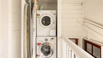 A laundry room with two stacked washing machines, a drying rack, and a bottle of detergent.