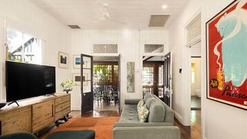 A living room with a television, sofa, and ottoman. There is a dining area with chairs and a table.