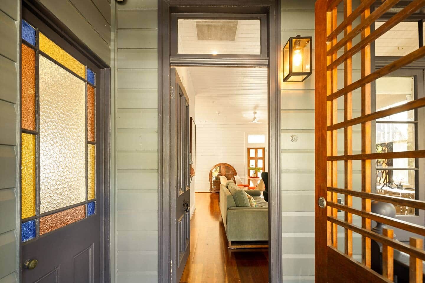 A hallway with a wooden door, a glass door with colorful stained glass, and a sofa in the background.