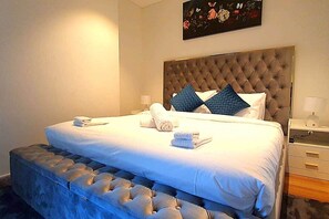A hotel room with a large bed, a tufted headboard, a bedside table with a lamp, and a wall-mounted painting. - Luxury Skytower 2BR River Views | Parking Sleeps 5 (Brisbane City)