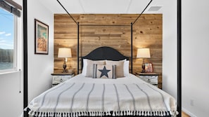 A bedroom with a bed, two bedside tables, a nightstand, a wall-mounted lamp, a framed picture, and a window. - Rawhide Ranch by Avantstay Hot Tub + Fenced Yard + Grill Mountain Views + Near Park (Pioneertown)