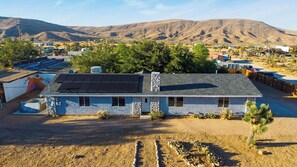 A single-story house with a sloped roof, solar panels, and a stone chimney. - Rawhide Ranch by Avantstay Hot Tub + Fenced Yard + Grill Mountain Views + Near Park (Pioneertown)