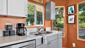A kitchen with a double sink, a coffee maker, and a view of the outdoors. - Rawhide Ranch by Avantstay Hot Tub + Fenced Yard + Grill Mountain Views + Near Park (Pioneertown)