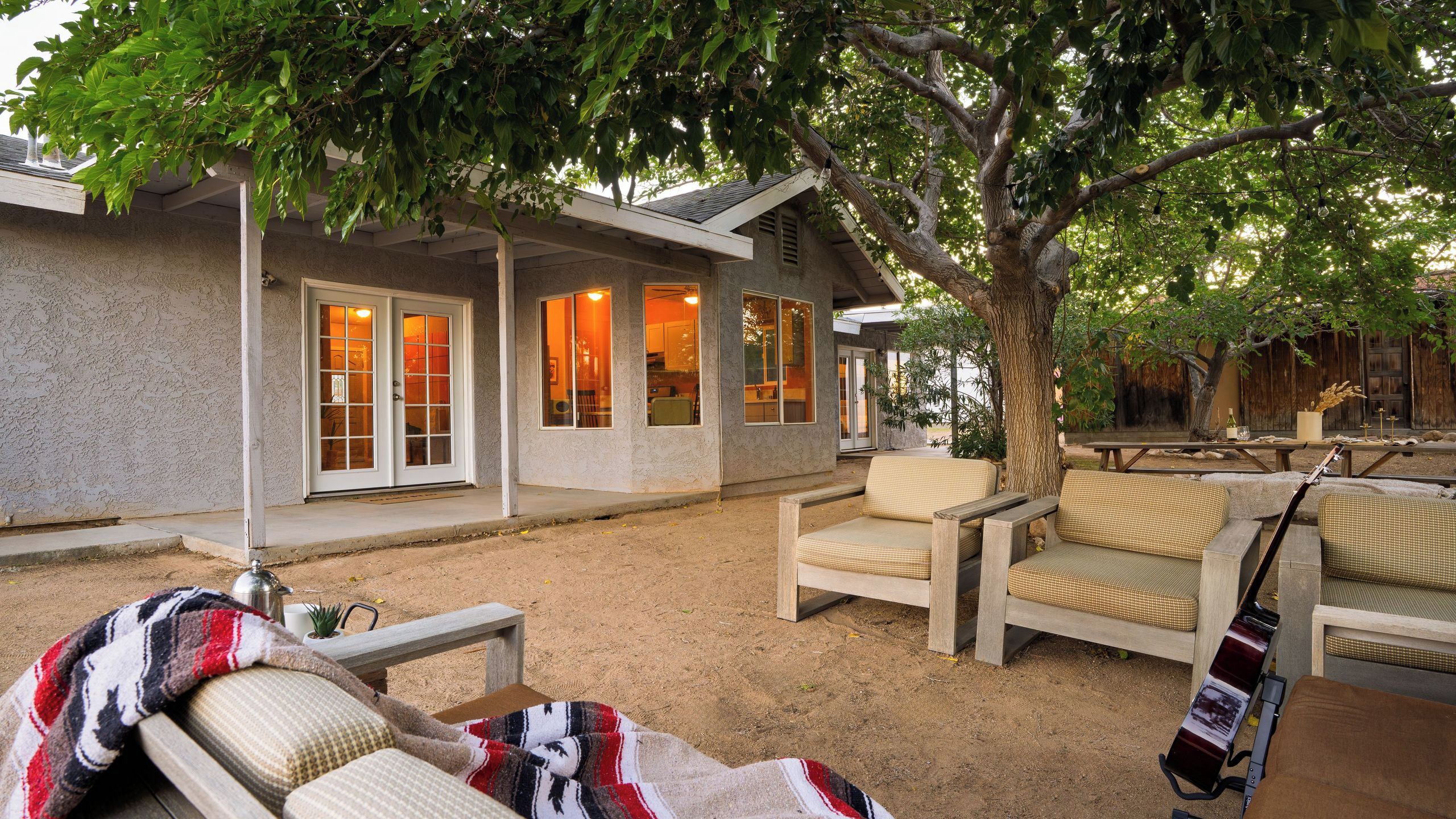 A house with a covered patio, outdoor seating, and a large tree providing shade.