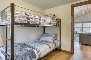 Ein Etagenbett mit einer unteren Liege und einer Matratze auf dem Boden, ein Fenster mit Blick und eine Holztür.