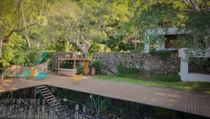 A wooden deck with a stone wall and a covered seating area with chairs. - Casa Los Mangos - Private Dock on the Lake (Santa María Del Oro)