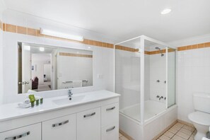 Ein modernes Badezimmer mit einem weißen Waschtisch, einem großen Spiegel, einer Duschkabine und einer Toilette.