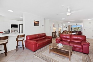 A living room with a red leather sofa, a wooden coffee table, and a kitchen area with white cabinets and appliances. - 2 Bedroom Apartment on the Burleigh Esplanade! (Gold Coast)
