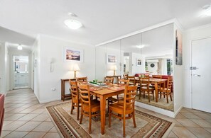 A dining area with a wooden table and chairs, a rug, and a large mirror reflecting the room. - 2 Bedroom Apartment on the Burleigh Esplanade! (Gold Coast)