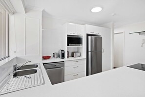 A modern kitchen with stainless steel appliances, white cabinetry, and a double sink. - 2 Bedroom Apartment on the Burleigh Esplanade! (Gold Coast)