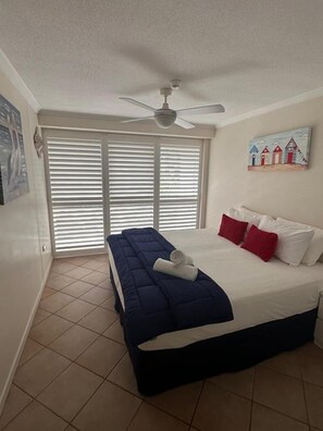 Ein Schlafzimmer mit einem Bett, einem Deckenventilator, einem Fenster mit Jalousien und einem Bild an der Wand.
