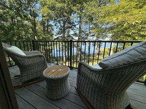 Ein Balkon mit Korbmöbeln, einem kleinen runden Tisch und Blick auf einen See.
