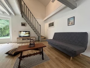 A living room with a wooden floor, a grey sofa, a wooden coffee table, a television, and a staircase. - The Landaise Barn - LAGLORIEUSE (LAGLORIEUSE)