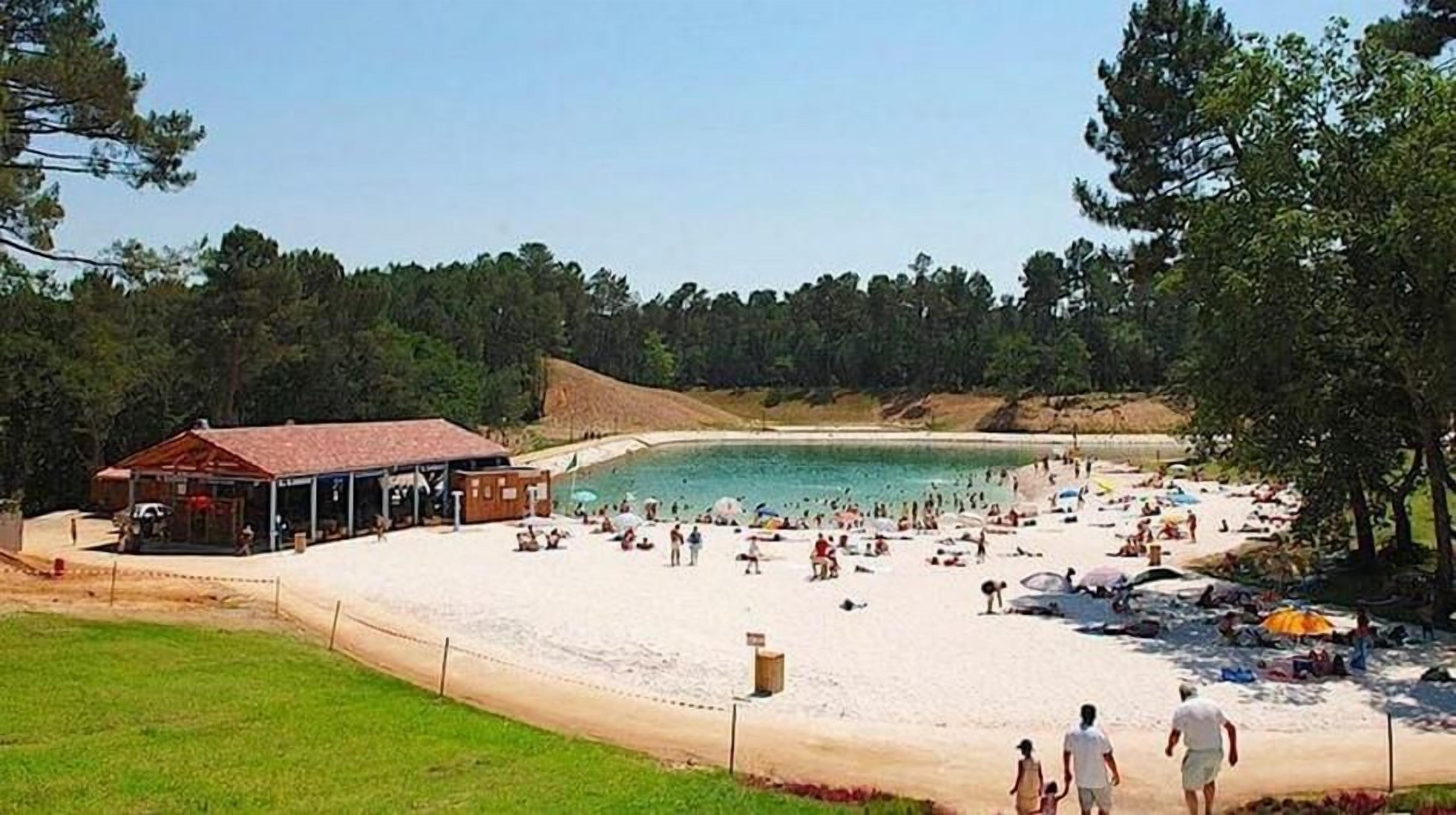 Una playa con un edificio, una zona arenosa y un fondo boscoso.