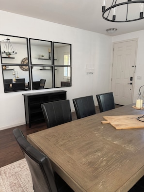 A dining area with a large wooden table, black chairs, and a wall-mounted mirror with shelves. - Windham Retreat (Chico)
