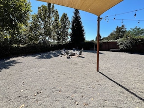 An outdoor seating area with a gravel ground, surrounded by trees and a wooden fence. - Windham Retreat (Chico)