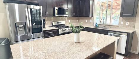 A kitchen with dark cabinets, stainless steel appliances, a granite countertop, and a central island with bar stools.
