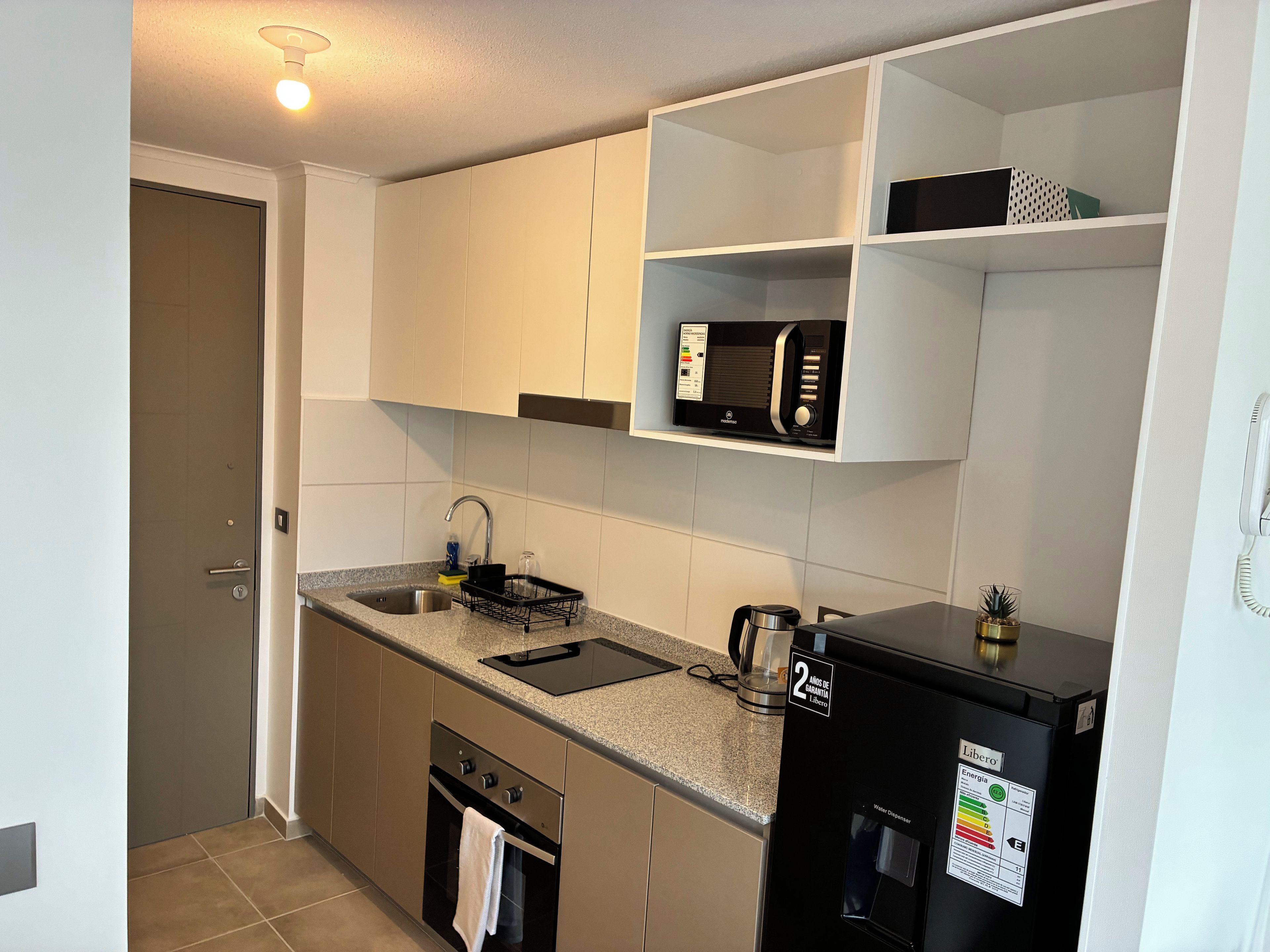 A compact kitchen with a built-in microwave, a water dispenser, and a coffee maker.