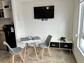 A modern kitchen with a dining area, a flat-screen TV mounted on the wall, a water dispenser, and a small plant. - The perfect studio for your next stay in Concepción (Concepción)