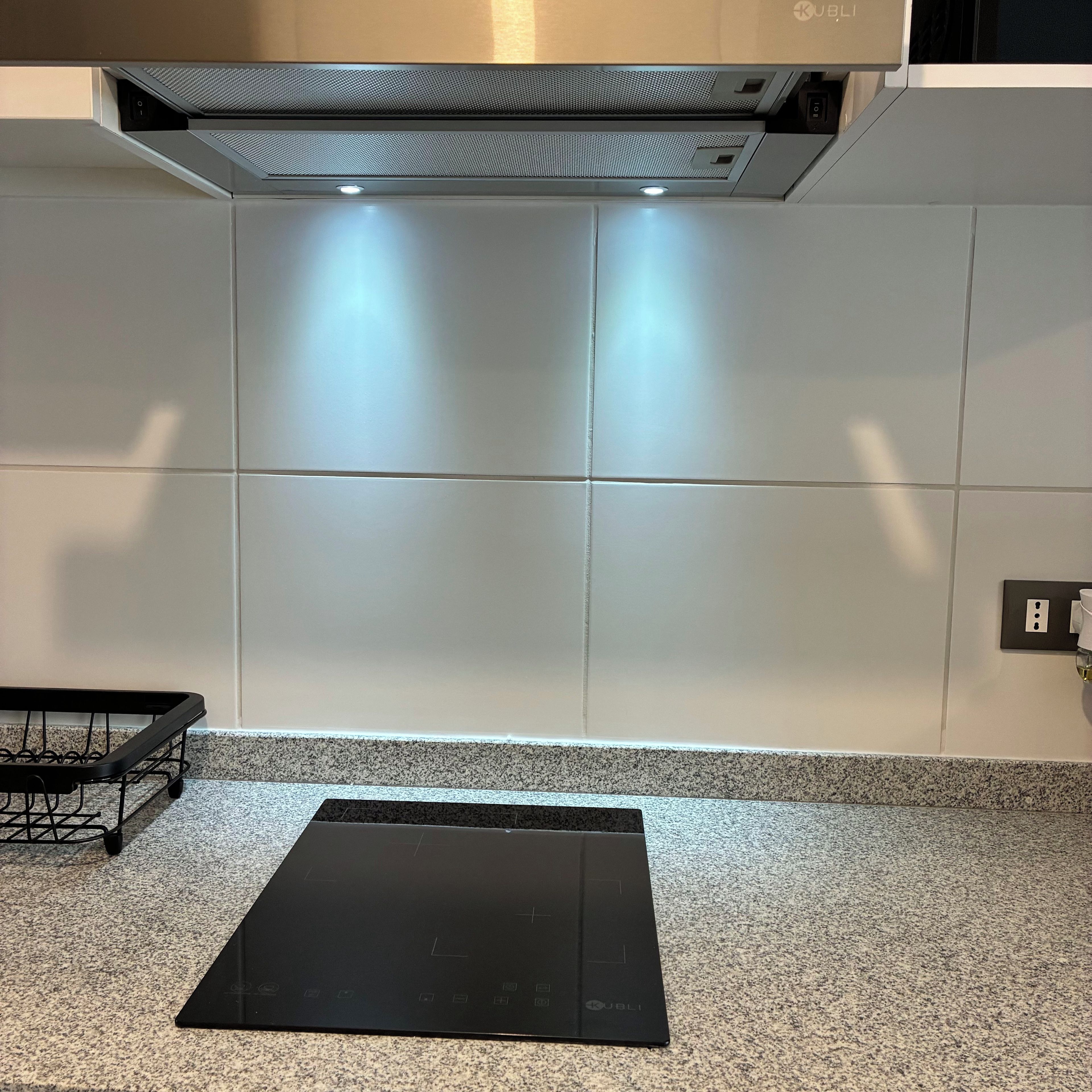 Una cocina con tope de inducción negro, azulejos blancos y campana extractora de acero inoxidable.