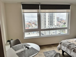 A room with a large window, a bed, a dining table with chairs, and a remote control on the table. - The perfect studio for your next stay in Concepción (Concepción)