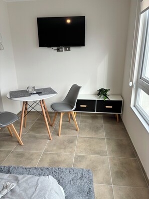 A modern, compact living space with a flat-screen TV mounted on the wall, a dining table with chairs, a bench with storage, and a large window providing natural light. - The perfect studio for your next stay in Concepción (Concepción)