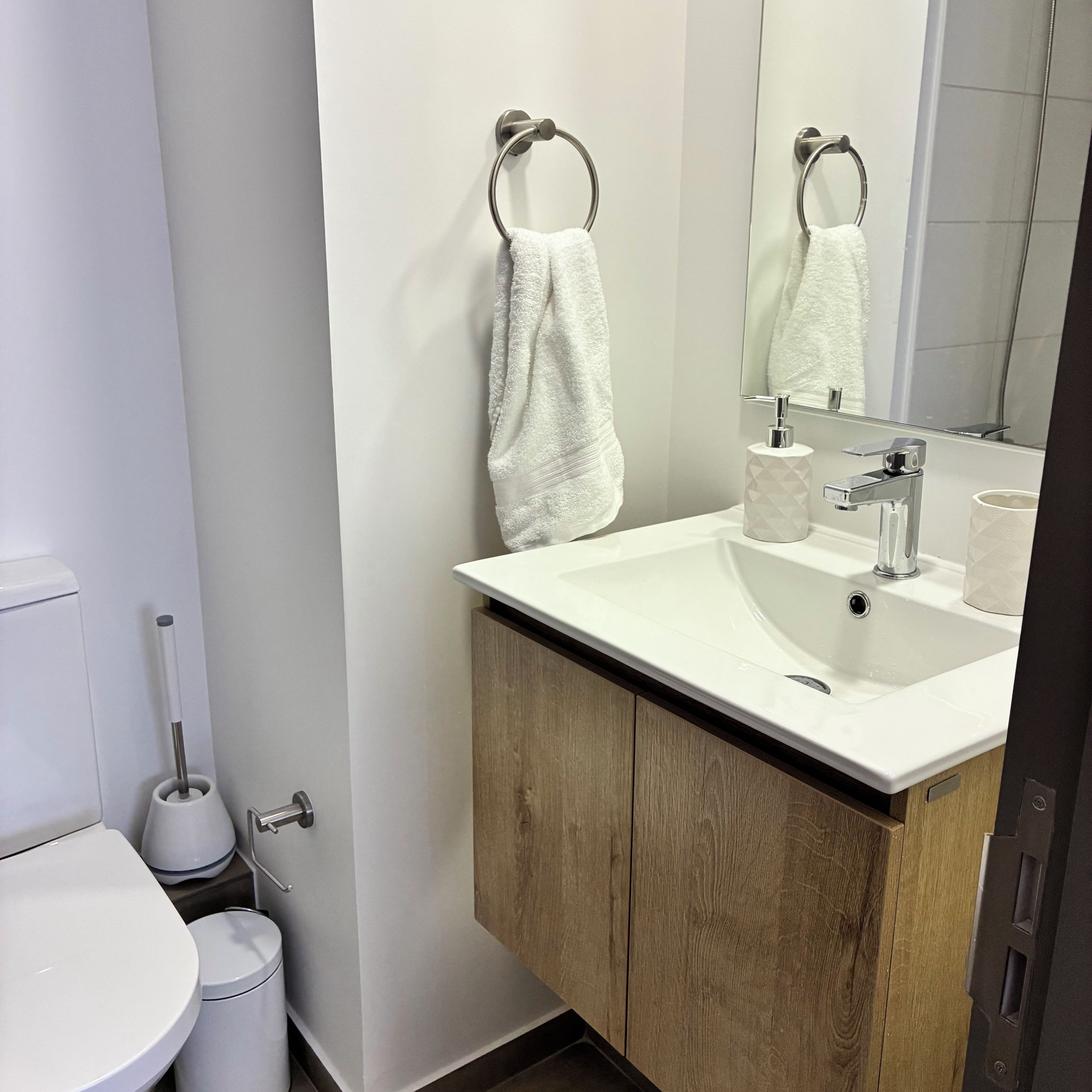 Un baño moderno con lavamanos blanco, mueble de madera y un espejo.