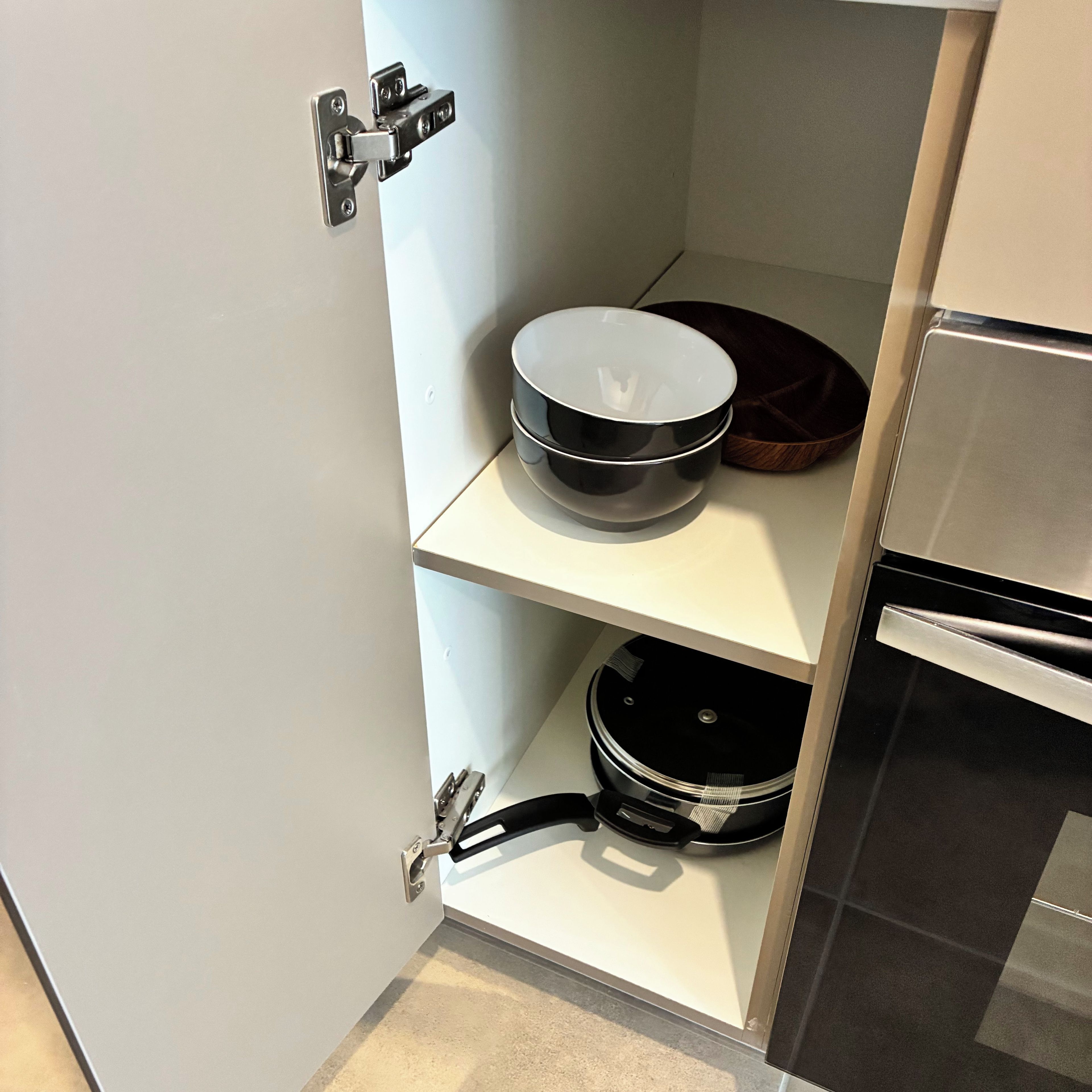 A kitchen with a white cabinet, a black pot on the top shelf, and a stove on the bottom shelf.