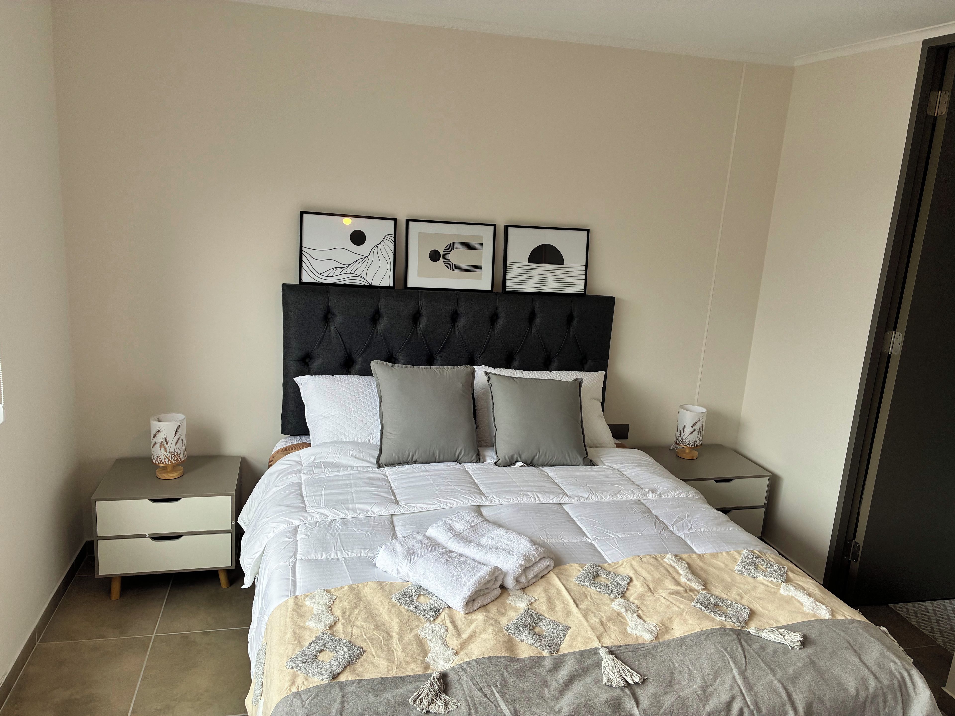 A neatly made bed with a quilt and pillows, a bedside table with a lamp, and framed artwork on the wall.