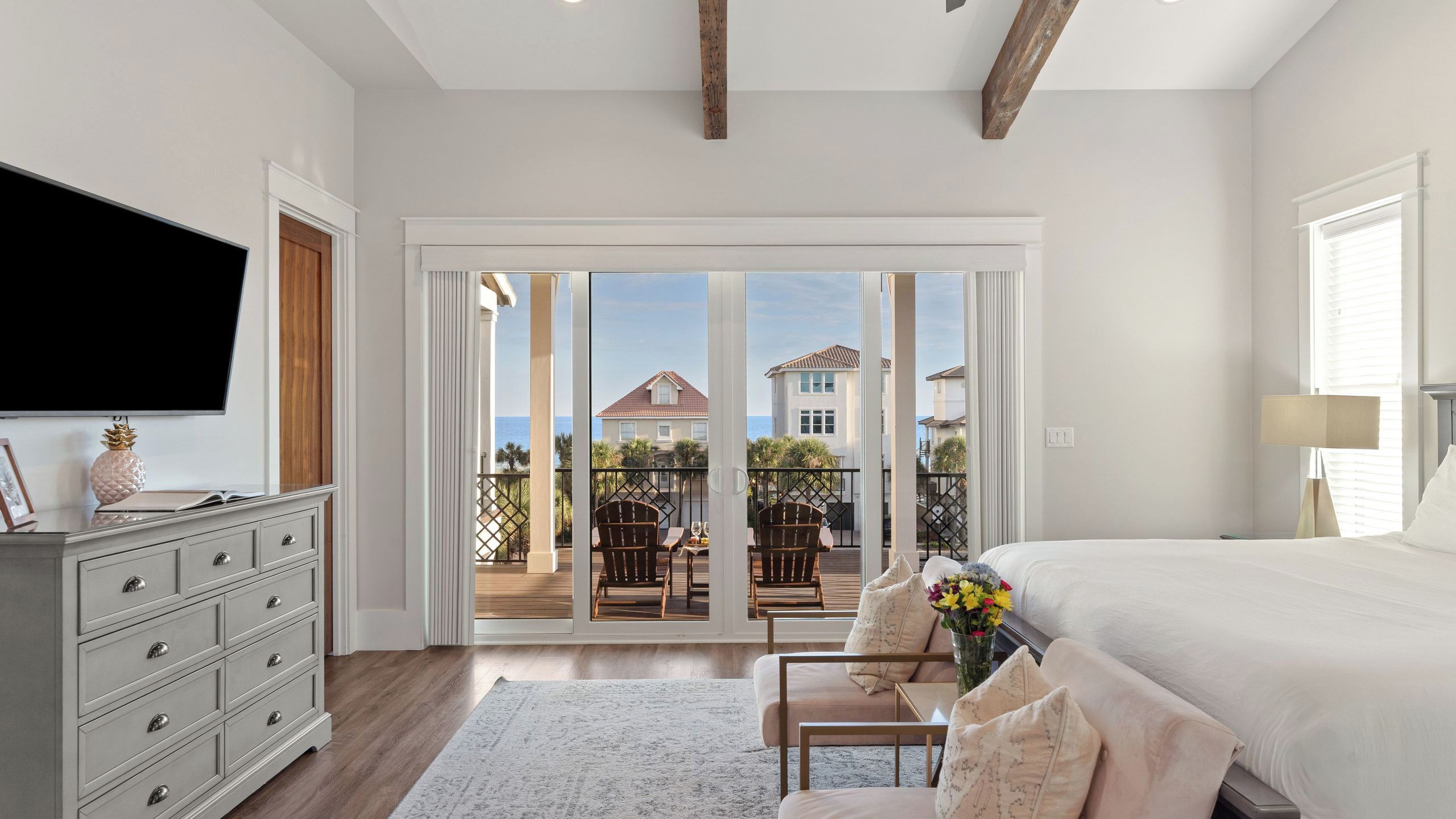 Une chambre dotée d’un grand lit, d’une commode, d’un téléviseur et offrant une vue sur un balcon aménagé avec du mobilier d’extérieur.