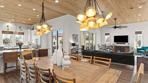 A modern kitchen with wooden cabinets, a dining area with a wooden table and chairs, and a living area with a sofa and a TV. - Sea E O by Avantstay Sleeps 24 Private Pool + Elevator Gulf Views + Steps to the Beach (Destin)