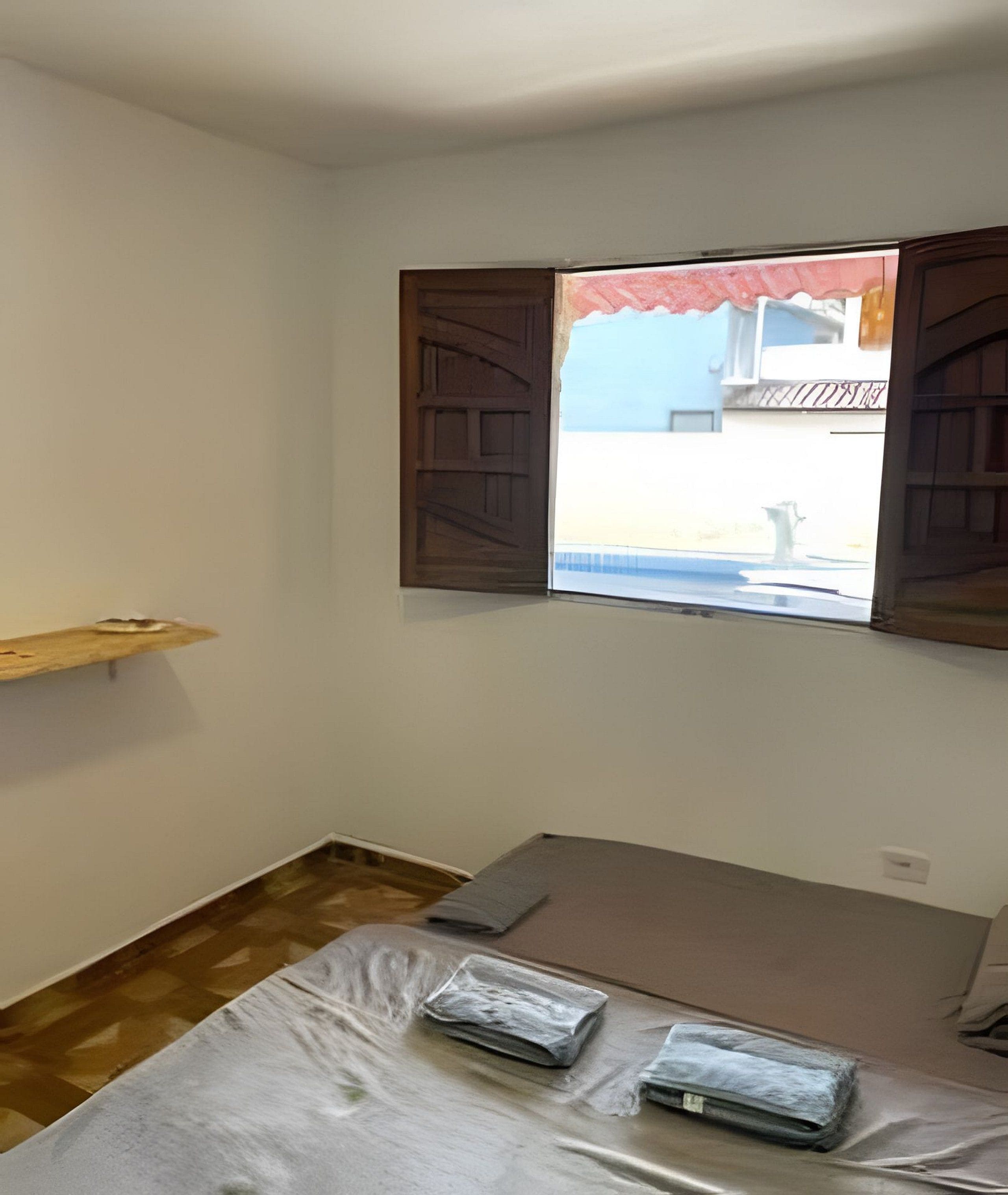 Quarto com janela, prateleira de madeira e cama com colchão e travesseiros.