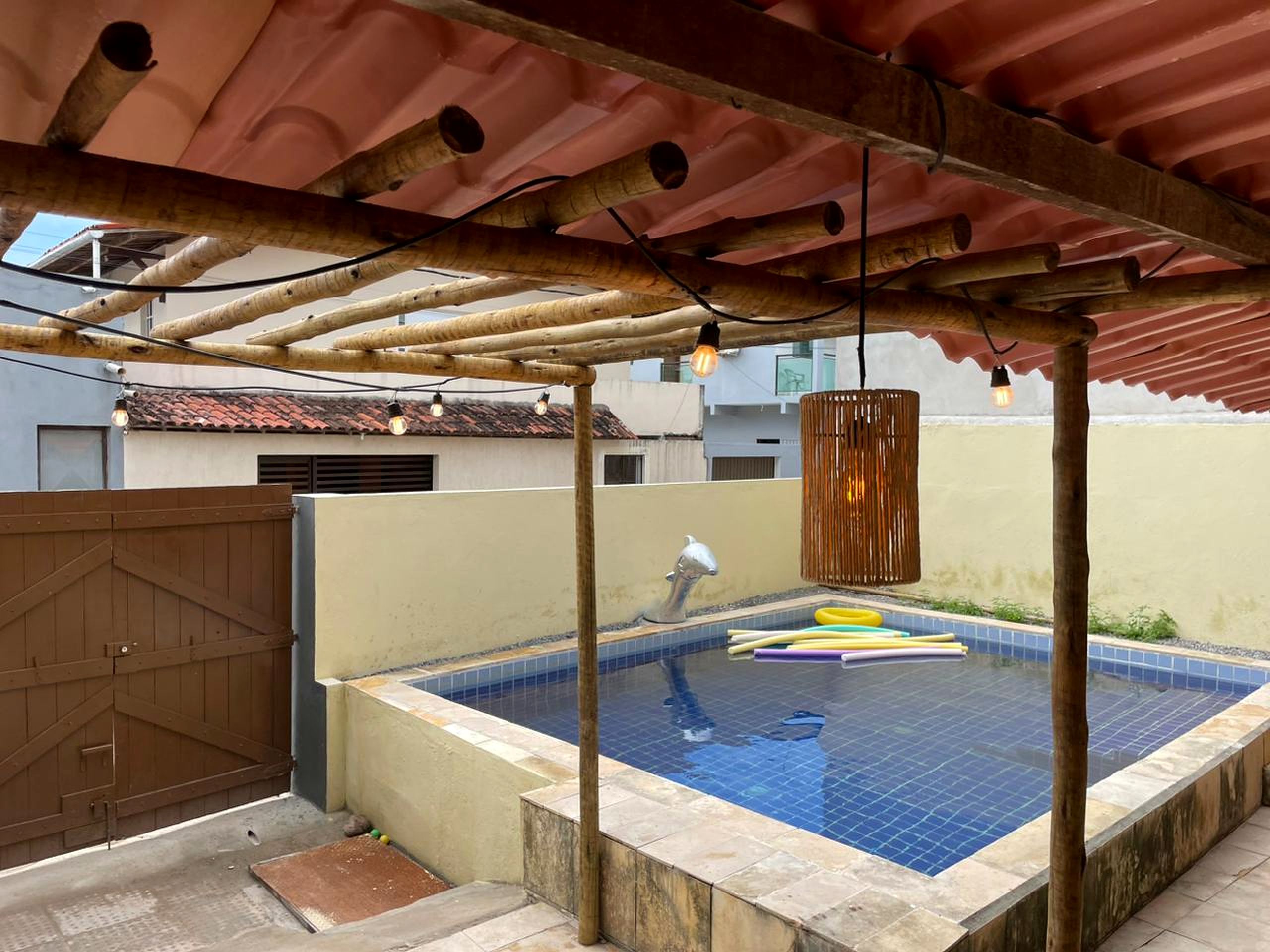Una piscina en la azotea con una pérgola de madera encima, rodeada por un muro bajo y un portón de metal.