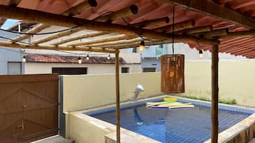 Una piscina en la azotea con una pérgola de madera encima, rodeada por un muro bajo y un portón de metal.