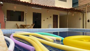 Una piscina con tubos inflables de colores y un área de terraza techada.