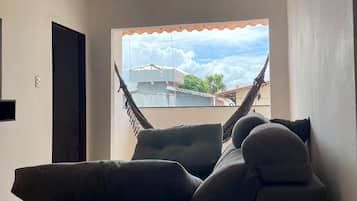 Una habitación con una hamaca, un sofá y vistas a edificios a través de una ventana.
