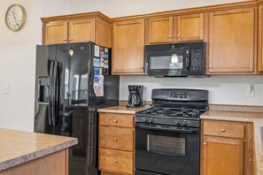 Una cocina con armarios de madera, un refrigerador de acero inoxidable, un microondas, una estufa y una cafetera.