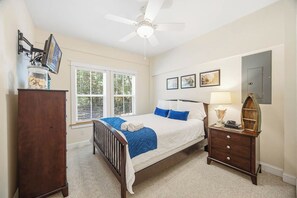 Un dormitorio con cama, mesita de noche, cómoda, ventilador de techo y ventana con persianas.