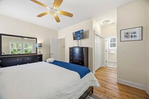 Ein Schlafzimmer mit einem Bett, einem Schminktisch, einem Wandfernseher und einem Deckenventilator.