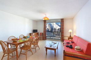 Ein Zimmer mit Esstisch, Stühlen, einer Couch, einem kleinen Tisch, einem Fernseher und Bergblick.