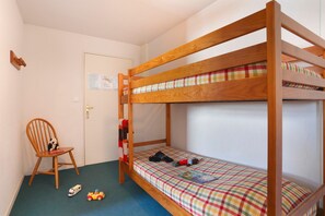Ein Schlafzimmer mit Etagenbetten, einem Holzrahmen, einer Karo-Bettdecke, einem Stuhl mit einem Stofftier und einer Tür mit einem Hinweis.