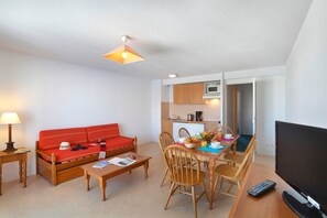 A compact living space with a sofa, dining table, chairs, a television, and a kitchenette. - Studio Vue Pyrénées | Piscine Chauffée | Sauna (Germ)