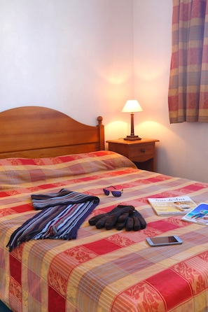 Un lit bien fait, recouvert d’une couverture à rayures, une lampe de chevet, une paire de lunettes de soleil, une paire de gants et un téléphone intelligent posés sur le lit.