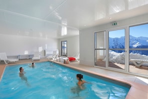 Ein Hallenbad mit freiem Blick auf schneebedeckte Berge durch große Fenster.