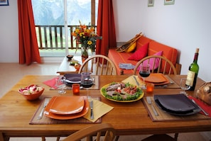 Ein Esstisch ist für eine Mahlzeit gedeckt, mit Tellern, Besteck und Gläsern, einer Weinflasche und einer Schüssel mit Gemüse.