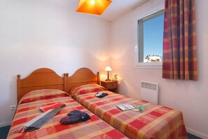 Ein Doppelbett mit Holz Kopfteil, ein Nachttisch mit Lampe, ein Fenster mit Vorhängen und ein Blick auf Gebäude im Freien.